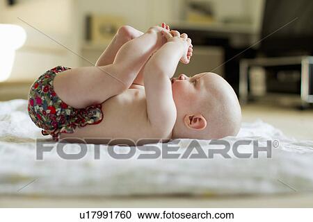 Stock Image - Baby girl lying on back playing with feet. Fotosearch