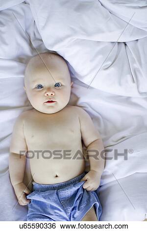Stock Photograph - Baby girl lying on bedclothes. Fotosearch