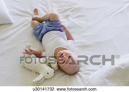 Baby girl lying on bedclothes with soft toy View Large Photo Image Stock Image - Baby girl lying on bedclothes with soft toy. Fotosearch