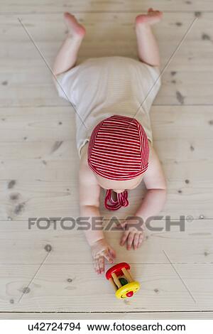 Picture - Baby girl lying on floor with toy. Fotosearch