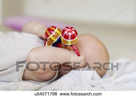 Stock Photo - Baby girl lying with rattle covering face. Fotosearch