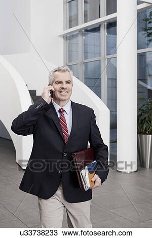 Stock Image - Businessman chatting on cellphone in office atrium. Fotosearch