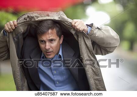 Stock Photo - Businessman holding up raincoat to shelter from rain. Fotosearch