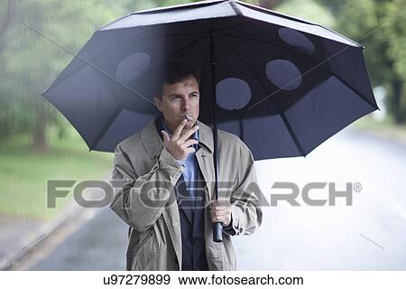 Businessman smoking cigarette under umbrella Stock Photo | u97279899 ...