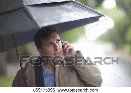 Stock Photograph - Businessman talking on cellphone whilst carrying umbrella. Fotosearch