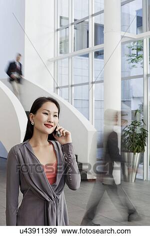 Businesswoman using cellphone in office atrium View Large Photo Image Stock Photo - Businesswoman using cellphone in office atrium. Fotosearch