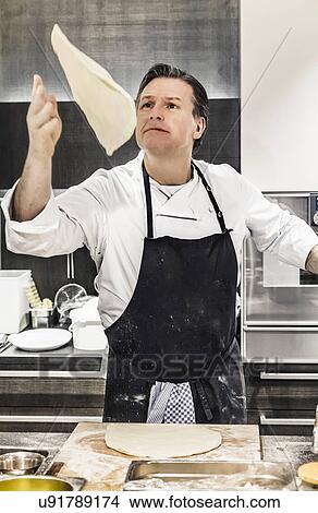 Picture - Chef throwing pizza dough mid air in commercial kitchen. Fotosearch