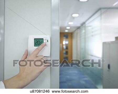Stock Photograph - Close up of office worker adjusting thermostat. Fotosearch