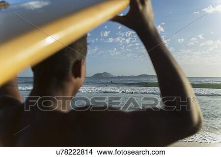 Picture - Close up of young man carrying surfboard, Rio De Janeiro, Brazil. Fotosearch