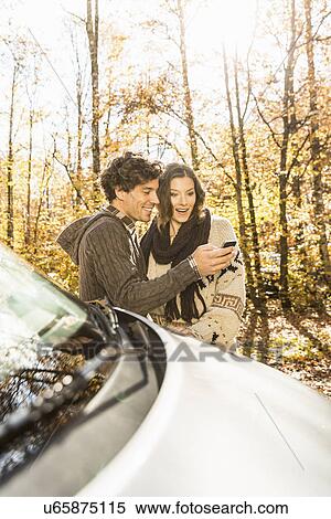 Stock Photography - Couple by car with cell phone. Fotosearch