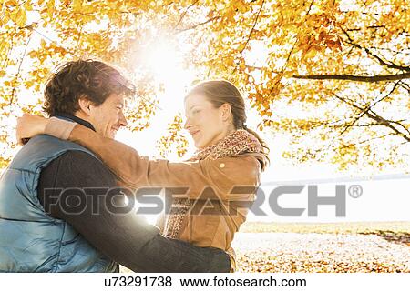 Stock Photo - Couple hugging by tree in sunlight. Fotosearch