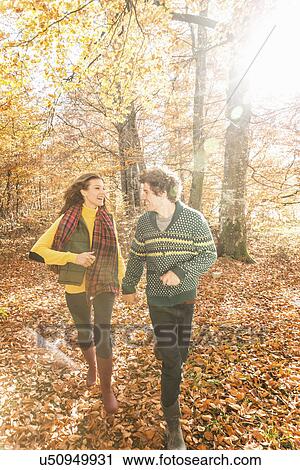 Stock Image - Couple running in forest holding hands. Fotosearch