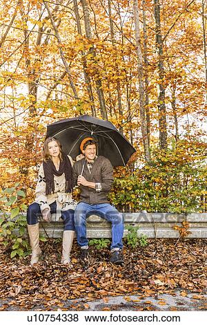 Couple sitting on fence with umbrella View Large Photo Image Stock Photo - Couple sitting on fence with umbrella. Fotosearch