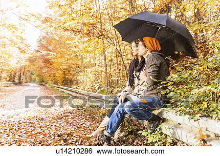 Couple sitting on fence with umbrella View Large Photo Image Stock Photograph - Couple sitting on fence with umbrella. Fotosearch