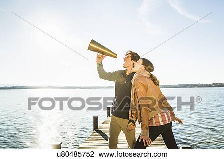 Stock Image - Couple using megaphone by lake. Fotosearch
