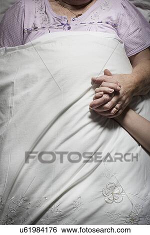 Stock Photograph - Cropped images of young woman holding sleeping senior woman's hand. Fotosearch