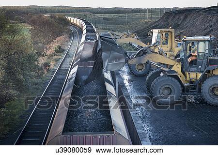 Stock Photo - Diggers loading coal onto train at surface coal mine at dawn. Fotosearch