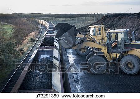 Stock Photo - Diggers loading coal onto train at surface coal mine at dawn. Fotosearch