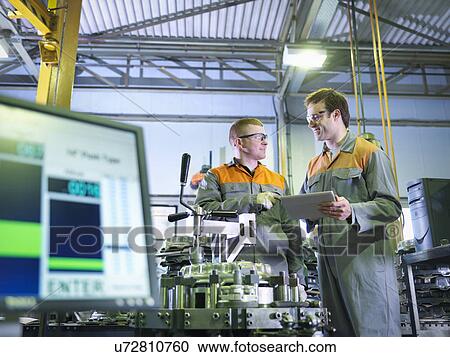 Stock Image - Engineer and apprentice using digital tablet at work station in factory. Fotosearch