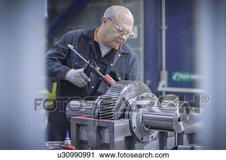 Stock Image - Engineer applying sealant to industrial gearbox in factory. Fotosearch