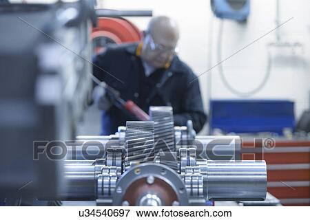 Stock Photo - Engineer applying sealant to industrial gearbox in factory. Fotosearch