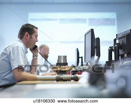 Stock Image - Engineer on the phone and using computer aided design in factory office. Fotosearch