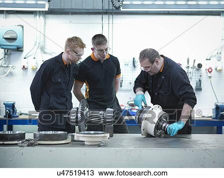 Stock Image - Engineer teaching apprentices in engineering factory. Fotosearch