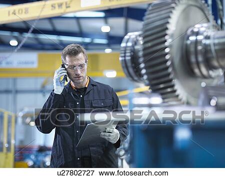Stock Photo - Engineer using mobile phone in engineering factory. Fotosearch