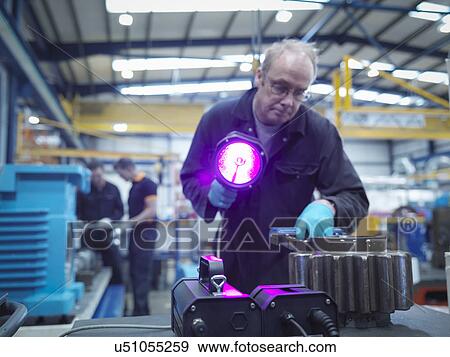 Stock Photo - Engineer using ultraviolet light to test for cracks in gear wheel. Fotosearch