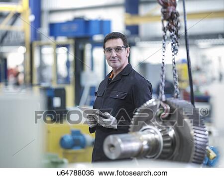 Stock Photograph - Engineer with gear wheel at work station in factory, portrait. Fotosearch