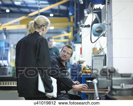 Stock Image - Engineers using computer to work on plans in engineering factory. Fotosearch