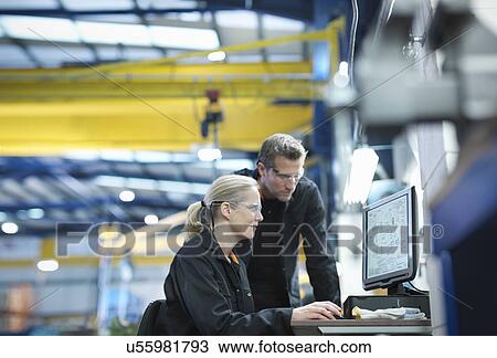 Stock Image - Engineers using computer to work on plans in engineering factory. Fotosearch