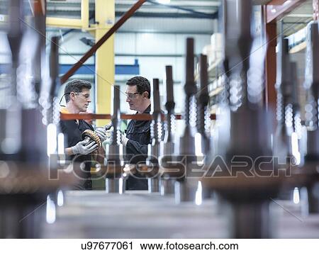 Stock Image - Engineers with parts in industrial gearbox factory. Fotosearch