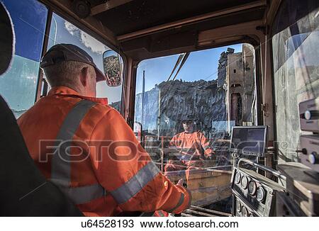 Stock Image - Excavator driver in digger cab at surface coal mine. Fotosearch