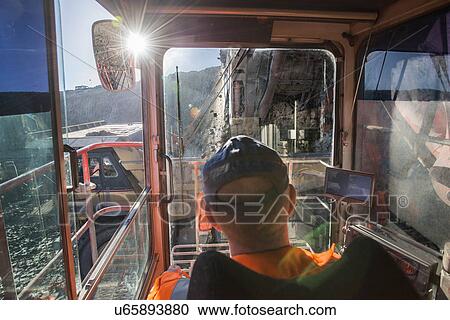 Stock Image - Excavator driver in digger cab at surface coal mine. Fotosearch