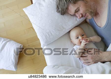Stock Photograph - Father and baby daughter on bed. Fotosearch