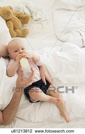 Stock Image - Father bottle feeding baby daughter. Fotosearch