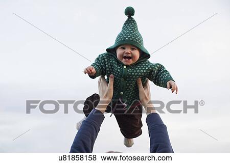 Stock Photo - Father lifting baby daughter against sky. Fotosearch