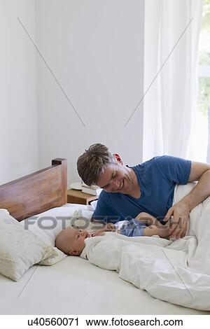 Stock Image - Father playing with baby daughter on bed. Fotosearch