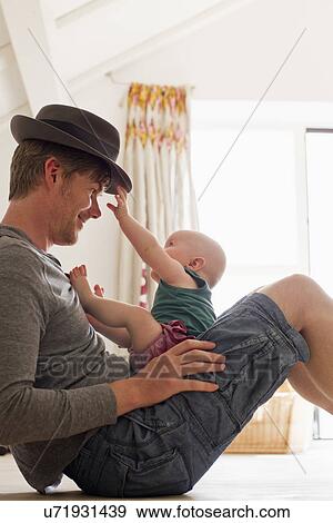 Stock Photo - Father wearing hat with baby sitting on his lap. Fotosearch