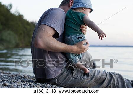 Stock Image - Father with baby daughter by lake. Fotosearch