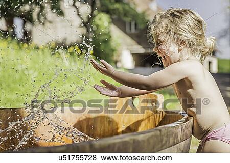 Stock Photo - Female toddler splashing hands in water barrel. Fotosearch