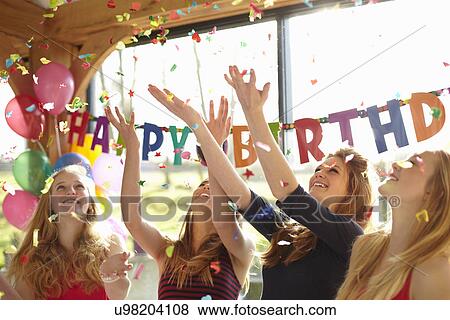 Stock Photo - Four teenage girls celebrating with confetti at birthday party. Fotosearch