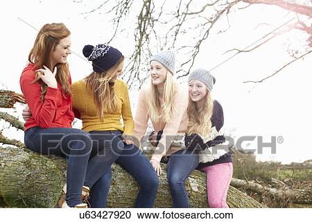 Stock Image - Four teenage girls sitting on top of tree trunk. Fotosearch