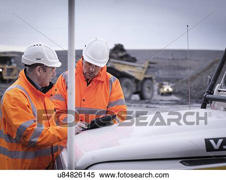 Stock Photography - Geologists discuss plans on digital tablet in surface coal mine. Fotosearch