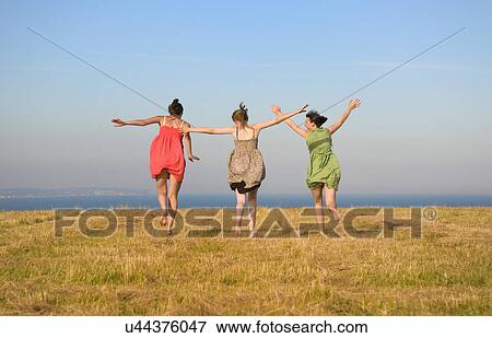Stock Photo - Girls dancing on grassy cliff top. Fotosearch