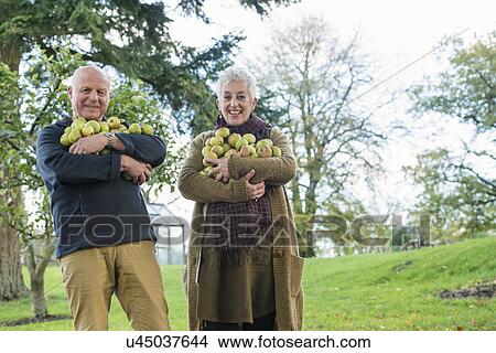 Picture - Happy senior couple with armful of apples. Fotosearch