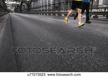 Stock Image - Legs of two men running over city bridge. Fotosearch