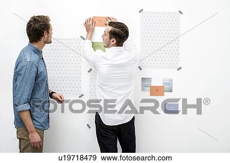 Stock Photo - Male colleagues preparing presentation on wall. Fotosearch
