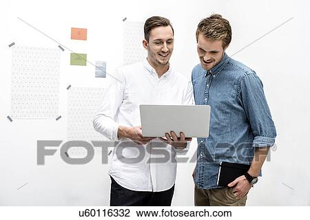 Stock Image - Male colleagues using laptop. Fotosearch